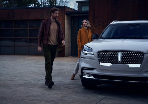 A man and a woman approaching a 2024 Lincoln Aviator® SUV, which illuminates certain lights when they are close | Northgate Lincoln in Port Huron MI