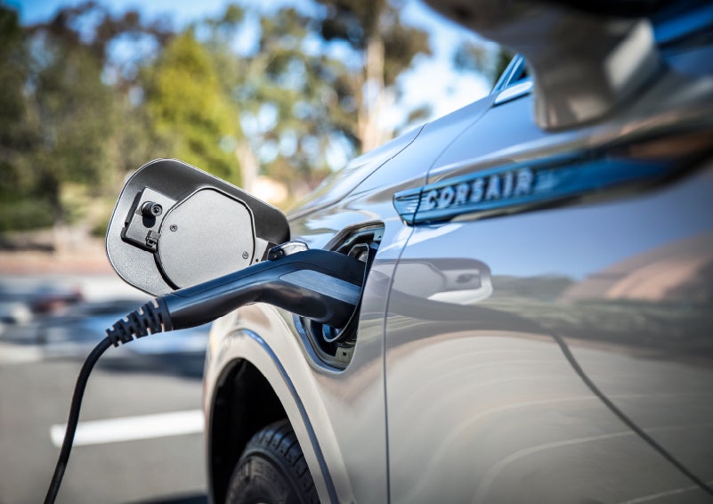 A Lincoln electric charger is plugged into a 2022 Lincoln Corsair Grand Touring port as the body reflects the surroundings of a sun-soaked parking lot | Northgate Lincoln in Port Huron MI