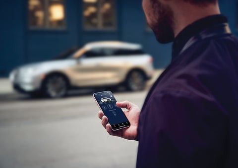 A person is shown interacting with a smartphone to connect to a Lincoln vehicle across the street. | Northgate Lincoln in Port Huron MI