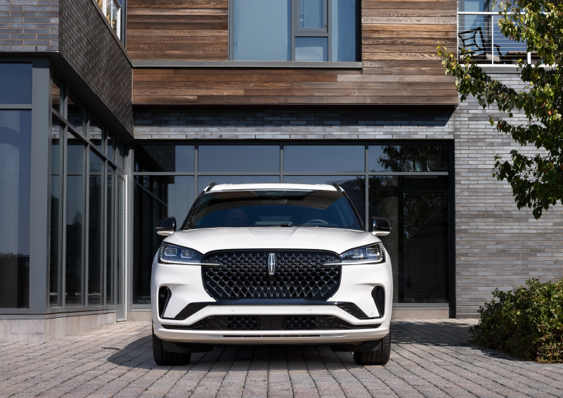 A white 2025 Lincoln Aviator® SUV is shown parked outside a modern building with gray brick and wood accents. | Northgate Lincoln in Port Huron MI