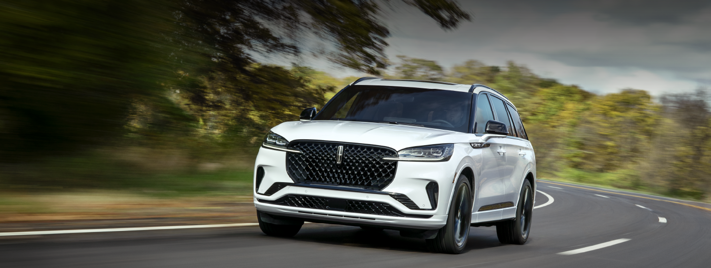 A white 2025 Lincoln Aviator® SUV is being driven down a road lined with trees. | Northgate Lincoln in Port Huron MI