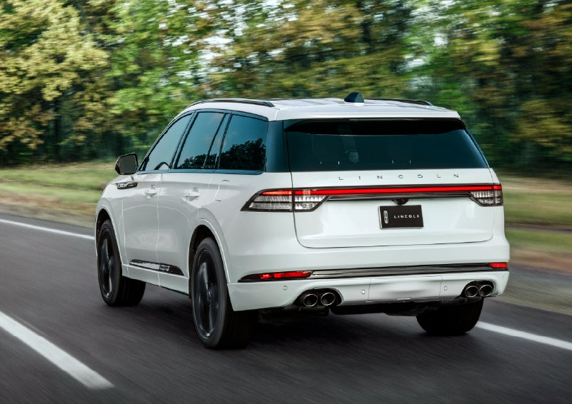 A white 2026 Lincoln Aviator® SUV is being driven away down a road lined with colorful trees. | Northgate Lincoln in Port Huron MI