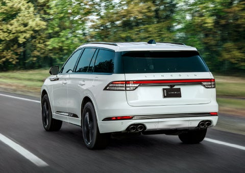 A white 2026 Lincoln Aviator® SUV is being driven away down a road lined with colorful trees. | Northgate Lincoln in Port Huron MI