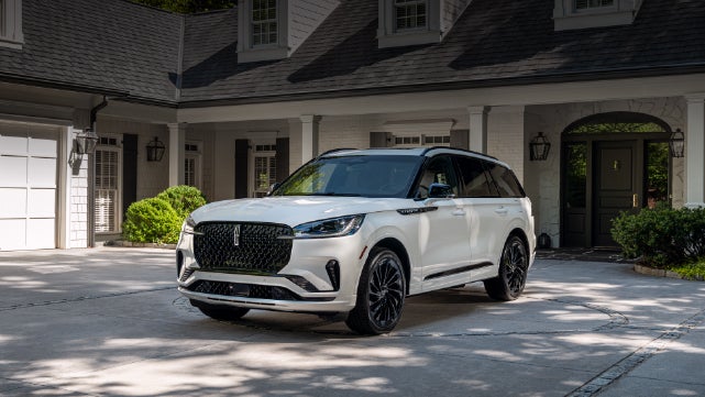 A white 2026 Lincoln Aviator® SUV is parked in the driveway of a luxury home. | Northgate Lincoln in Port Huron MI