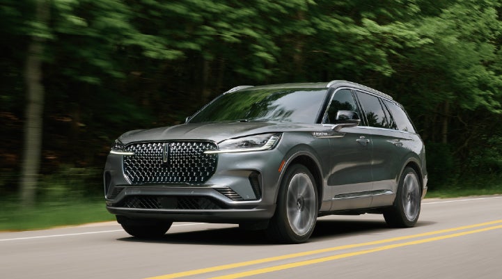 A 2027 Lincoln Aviator® SUV is being driven down a road lined with trees. | Northgate Lincoln in Port Huron MI